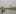 A man seen from behind stands in a small boat and rows on the Congo river. There are habitations on the shore in front of him.